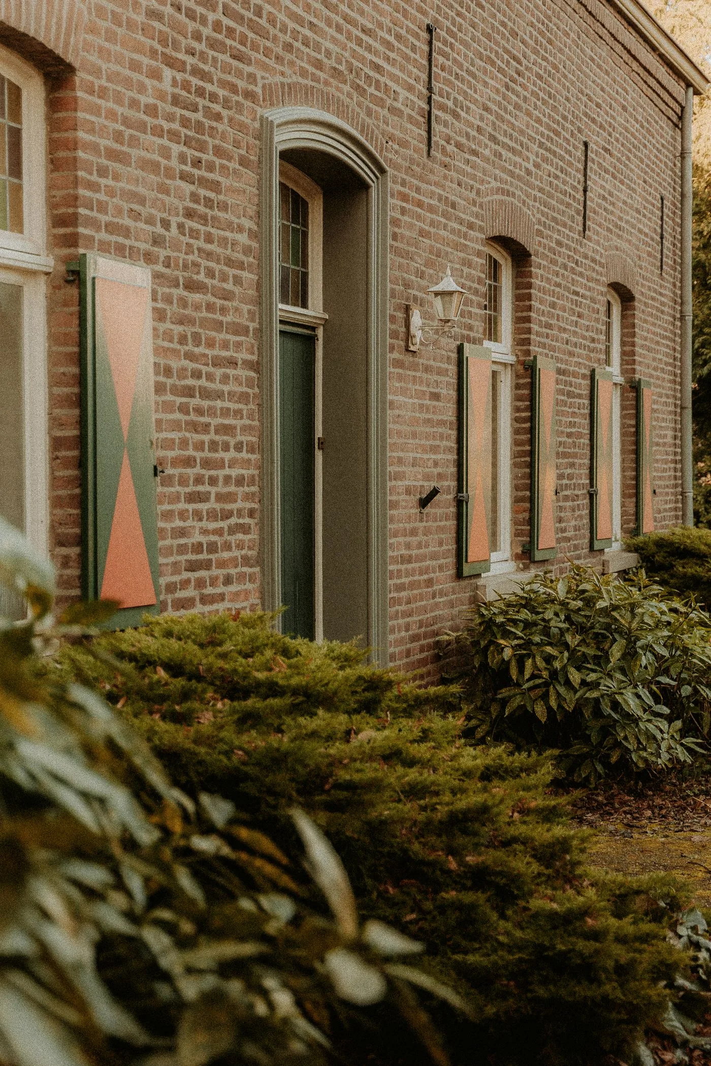 Echte foto van een Nederlandse bakstenen woning met groene en terracotta luiken en een grijsgroene deur
